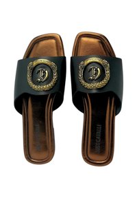 Sandales à glissière noires avec une large bride ornée d'un emblème circulaire doré et d'un motif chaîne. Semelles intérieures brunes, forme carrée à l'avant.