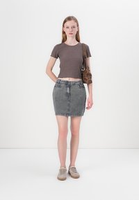 Šedý žebrovaný cropped top v kombinaci s vybledlými džínovými mini sukní. Modelka má na sobě světle šedé tenisky a nese hnědou crossbody tašku.