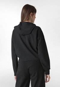 Svart kort hoodie med en stor huva, lös passform och ribbade ärmslut. Materialet verkar mjukt, med en slät textur och inget synligt mönster.