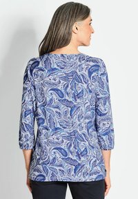 Blauwe en paarse top met paisleypatroon, driekwart mouwen, ronde hals en zachte stoftextuur. Het ontwerp bevat ingewikkelde bladvormen.