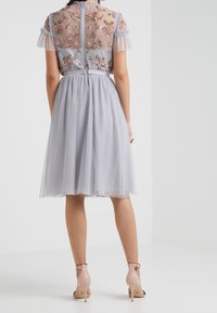 Vestido gris claro con mangas cortas y traslúcidas bordadas con flores, corsé ajustado y falda amplia con pliegues; combinado con sandalias de tacón nude.