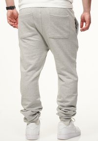 Graue Sweatpants mit einer lockeren Passform, elastischen Bündchen und zwei Gesäßtaschen. Kombiniert mit weißen Sneakers für einen lässigen Look.