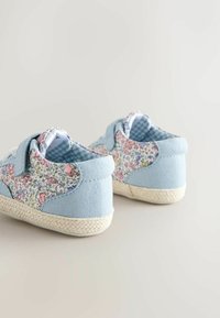 Vaaleansiniset kangaskengät, joissa on kukkakuvioiset kangaskoristeet, punotut juuttipohjat ja tarrakiinnitykset. Takakuvassa näkyvät kuvioidut yksityiskohdat ja pehmeät tekstuurit.