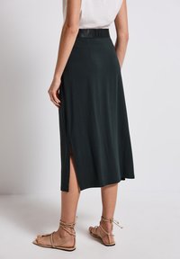 Tmavě zelená midi sukně s bočním rozparkem, vyrobená z měkké látky. Disponuje texturovaným černým pasem a jednoduchým, uvolněným designem.