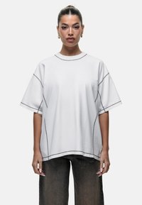Witte oversized t-shirt met korte mouwen en donkere stiksels langs de naden. Zachte stof met een ontspannen pasvorm.