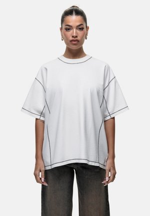 Witte oversized t-shirt met korte mouwen en donkere stiksels langs de naden. Zachte stof met een ontspannen pasvorm.