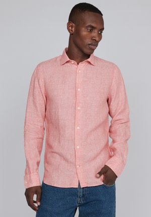 Camicia a maniche lunghe rosa chiaro in tessuto testurizzato, con colletto a punta e bottoni frontali; abbinata a jeans in denim blu.