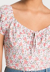 Květinový crop top v růžové a zelené barvě, s nařasenými rukávy, výstřihem ve tvaru lodičky a detailem na zavazování v přední části. Měkká, lehká tkanina s jemným vzorem.