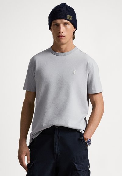 Lysegrå T-shirt med korte ærmer i et struktureret stof, med en lille logo på brystet, kombineret med mørke cargobukser og en marineblå hue.