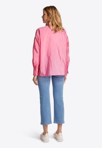 Blusa de satén rosa con una textura ligeramente arrugada y mangas largas, combinada con unos jeans de mezclilla recortados de color azul claro y zapatillas blancas.