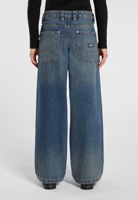 Wide-leg blue denim jeans with a high waist, featuring two back pockets and subtle fading. Stitched accents at the pockets and hem.