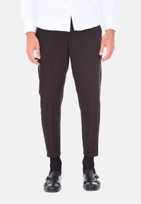 Pantaloni marroni su misura con una vestibilità slim, caratterizzati da una piega frontale e orli arrotolati, abbinati a scarpe nere e calzini scuri.