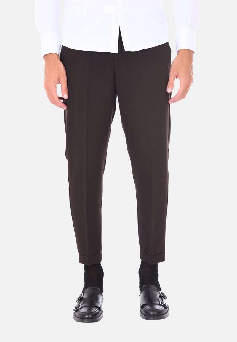 Pantaloni marroni su misura con una vestibilità slim, caratterizzati da una piega frontale e orli arrotolati, abbinati a scarpe nere e calzini scuri.