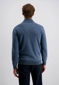 Blauer gestrickter Pullover mit hohem Kragen, figurnahem Schnitt, gerippten Säumen und Bündchen, glatter Textur und einem kreisförmigen Akzent auf dem Rücken.