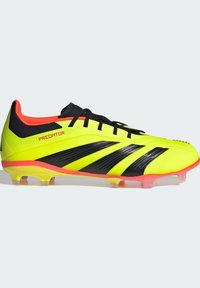 Chaussure de football jaune avec des rayures noires et des accents roses, présentant un dessus texturé et une semelle extérieure pour sol ferme avec des crampons transparents.
