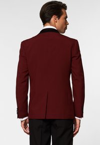 Blazer burdeos con solapa negra, con una abertura en la parte posterior y botones decorativos en las mangas, hecho de un tejido texturizado para ropa formal.