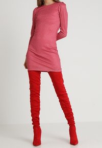 Robe à manches longues rayée rouge et blanche avec un design ajusté, associée à des bottes en suède rouge hautes jusqu'au genou. Texture lisse sur l'ensemble.