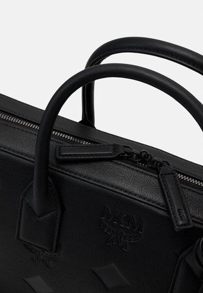 Sac à main en cuir noir avec deux poignées supérieures, fermeture zippée, logo MCM embossé et motifs en forme de diamant à l'avant.