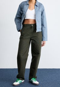 Giacca corta azzurro chiaro, canotta bianca, pantaloni leopardati verde scuro e scarpe da ginnastica con accenti verdi su un tappeto blu texture.