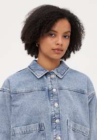 Heledad denim-jakk, heled bluus, kraega, hõbedaste nööpide sulgemisega, suurte ees mõnedega ja lõdva lõikega. Omab veidi pleekinud tekstuuri.
