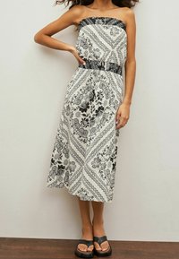 Trägerloses, schwarz-weißes Midi-Kleid mit floralen Motiven, das eine taillierte Taille und einen fließenden Rock hat, mit komplexen floralen und geometrischen Mustern.