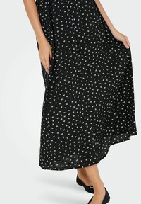 Schwarzes Blumen-Maxikleid mit kleinen weißen Blumenmustern, leichtes Material, lockere Passform und fließende Textur, kombiniert mit schwarzen Ballerinas.