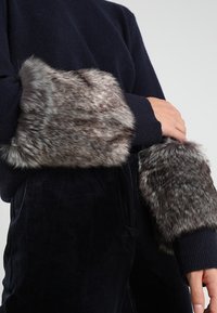 Polsini in pelliccia sintetica grigia con un motivo maculato, attaccati a un maglione blu navy, caratterizzato da dettagli a maglia a costine sui polsi.