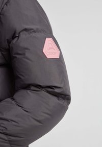 Puffjakkeærme i mørkegrå med en struktureret overflade. Har et pink gummilogo patch i hexagonal form på overarmen.