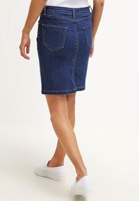 Denimpenningkjol i mörkblått med medelhög midja, två bakfickor och synliga sömdetaljer. Matchad med vita slip-on skor.