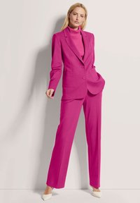 Fuchsia tailored suit featuring a blazer with two buttons and pockets, paired with a ribbed turtleneck, and straight-leg trousers.