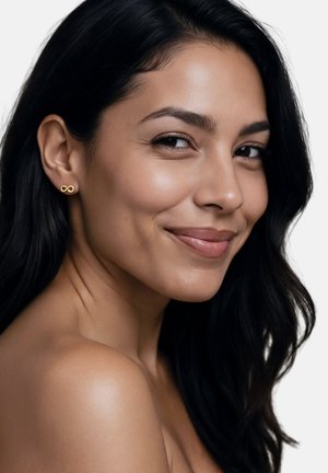 Tânără cu piele netedă și păr lung și închis la culoare zâmbește ușor, purtând cercei mici aurii în formă de simbol infinit pe un fundal simplu alb.