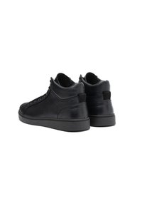 Une paire de baskets montantes noires en cuir avec des semelles plates, des panneaux latéraux texturés et des patchs de logo à l'arrière, montrées sous un angle arrière.