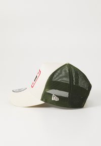 Gorra de béisbol con la parte delantera de tela crema y la parte trasera de malla verde oscura. Presenta una placa con el logo y un visor curvado. Ajuste regulable con cierre en la parte trasera.