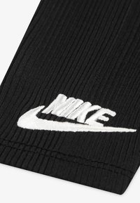 Tejido negro acanalado con un logo de Nike bordado en blanco. Diseñado con un acabado texturizado, que muestra una estética limpia y enfocada en el deporte.