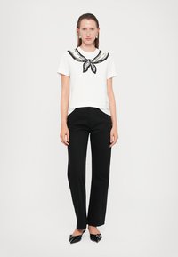 Cămașă albă cu mânecă scurtă, cu o guler în dungi negre și colorate, asociată cu pantaloni negri drept și pantofi negri lucioși.