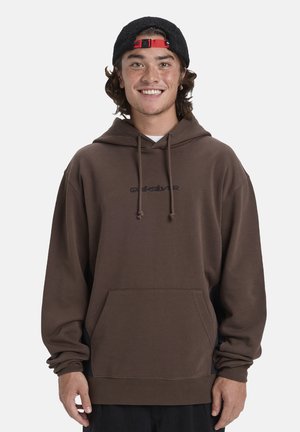 Brown hooded sweatshirt with a front pocket, drawstrings, and a black logo. Loose fit, soft fabric, and ribbed cuffs and hem.