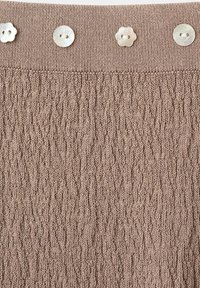 Tissu tricoté marron avec un motif côtelé et quatre boutons blancs cousus, deux ronds et deux en forme de fleur, le long du bord supérieur.