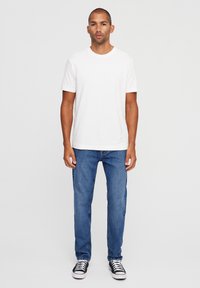 White short-sleeve T-shirt, blue jeans, black and white sneakers. The outfit features a classic fit with a smooth texture and simple design.