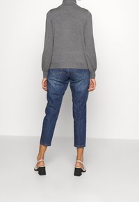 Pull en tricot gris à col haut associé à un jean droit bleu. Des sandales à talon bloc à brides complètent la tenue.