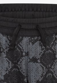 Szare spodnie w wężowy wzór posiadają czarny prążkowany pas z troczkami oraz subtelne teksturowane detale. Wzór imituje skórę węża.