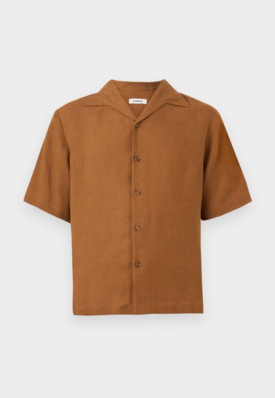 Καφέ πουκάμισο με κοντά μανίκια και κουμπιά, με γιακά τύπου κάμπινγκ, πέντε κουμπιά στην μπροστινή πλευρά, σε απλό ανοιχτό γκρι φόντο.