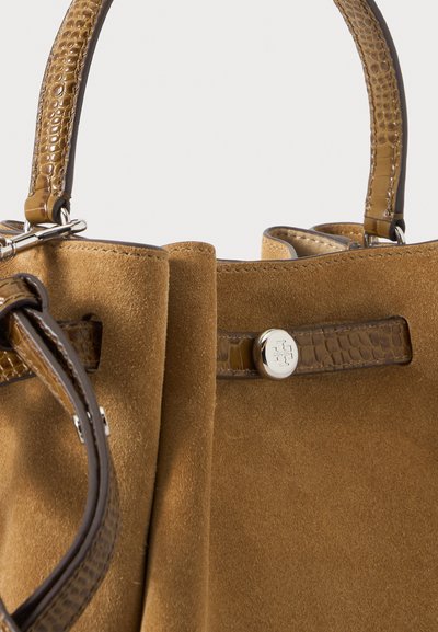Sac à main en daim marron avec des poignées en cuir texturé et des détails de sangle, équipé d'un fermoir rond en argent avec gravure de logo.