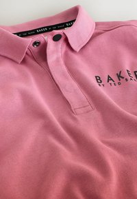 Rosa Poloshirt mit schwarzen Druckknöpfen und dem auf der Brust sowie im Krageninneren aufgedruckten Logo "BAKER BY TED BAKER".