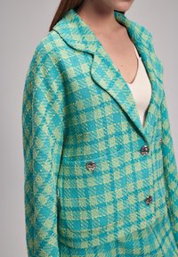 Blazer a scacchi turchese e verde con colletto a punte, dotato di bottoni argentati e tessuto testurizzato. Silhouette aderente con tasche.