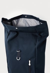 Granatowy plecak typu roll-top wykonany z trwałego materiału, z przednią kieszenią na zamek błyskawiczny, srebrnymi akcesoriami oraz gładkim szarym wnętrzem.