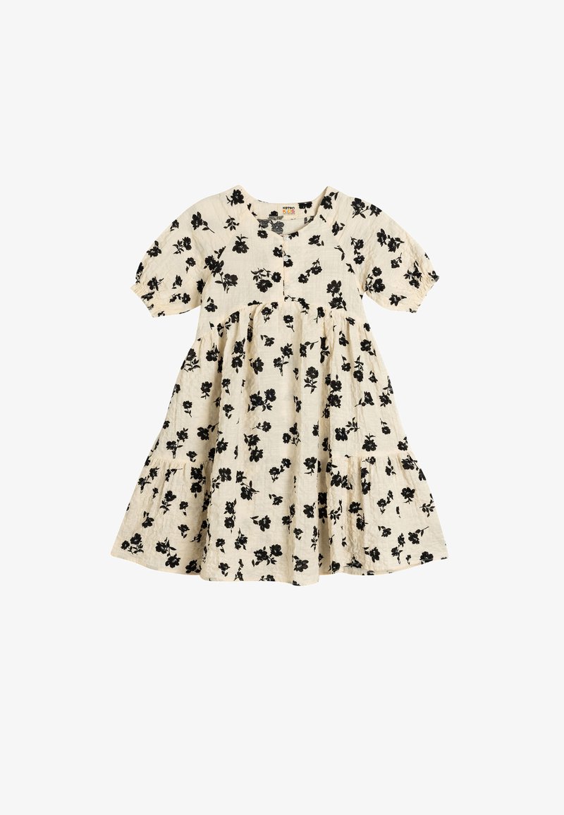 Blommig klänning i beige med svart blommönster, korta puffärmar, knapstängning och en volangkjol med fickor. Tillverkad av bomullsmaterial.