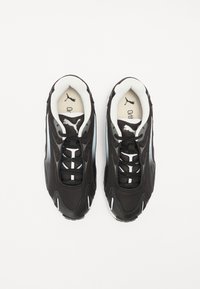 Baskets de sport noires avec une tige en maille et cuir, dotées d'une semelle épaisse, de lacets blancs et du logo Puma sur la languette et le panneau latéral.