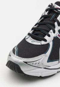 Black and silver athletic shoe with mesh upper, synthetic accents, and textured sole. Features laces and distinct logo detail.