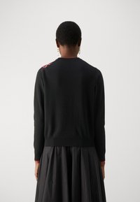 Black knitted sweater featuring a fitted ribbed hem and cuffs, with pink floral embroidery on the left shoulder.