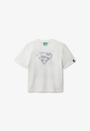Biała koszulka z krótkim rękawem z srebrnym logo Supermana umieszczonym na środku klatki piersiowej, okrągły dekolt i mała czarna metka na lewym rękawie.